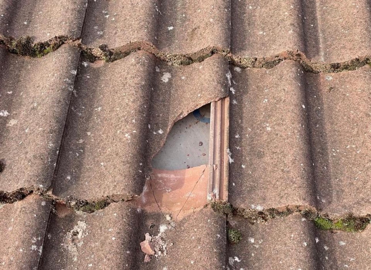 Damaged roof tile with a broken clay tile creating an opening, exposing the underlayment beneath