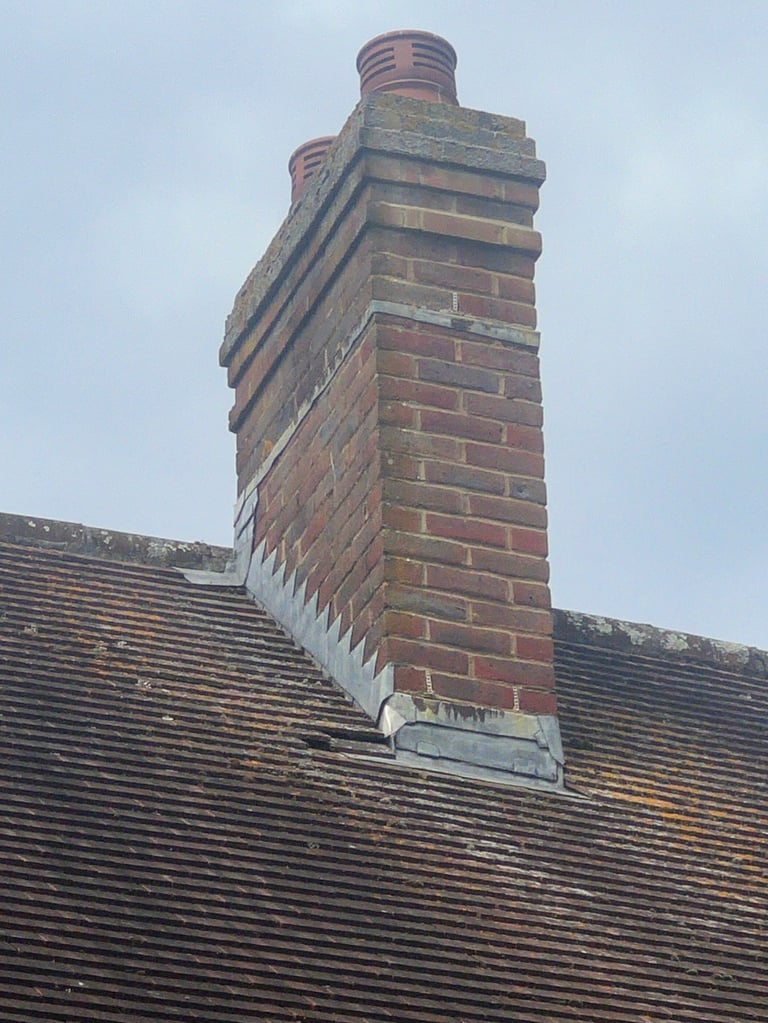 Tall red brick chimney with stepped cap rising above a dark slate tile roof against a light sky