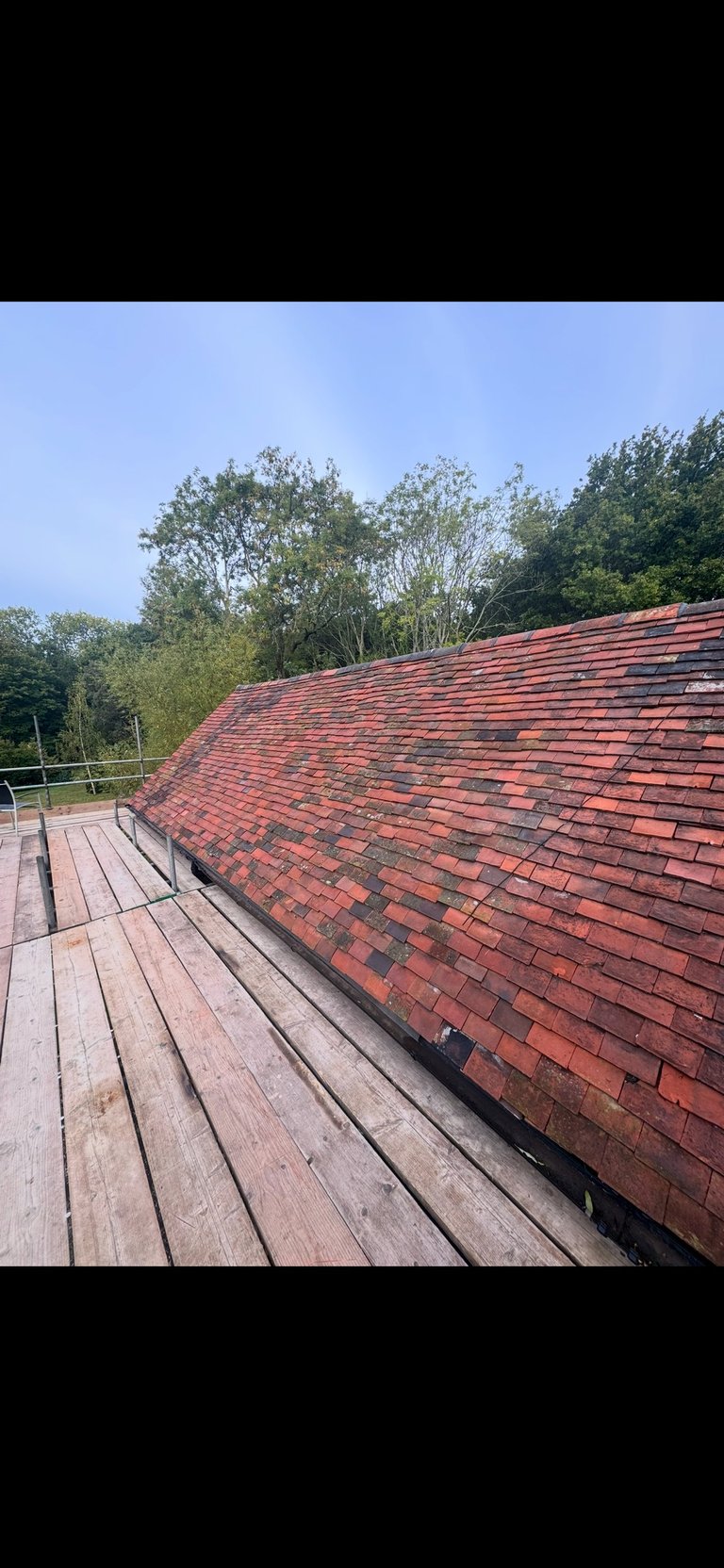 Wooden deck overlooking a red brick roof with forested hillside in background under clear sky
