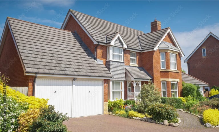 Two-story brick house with white garage, slate roof, and landscaped garden on sunny day